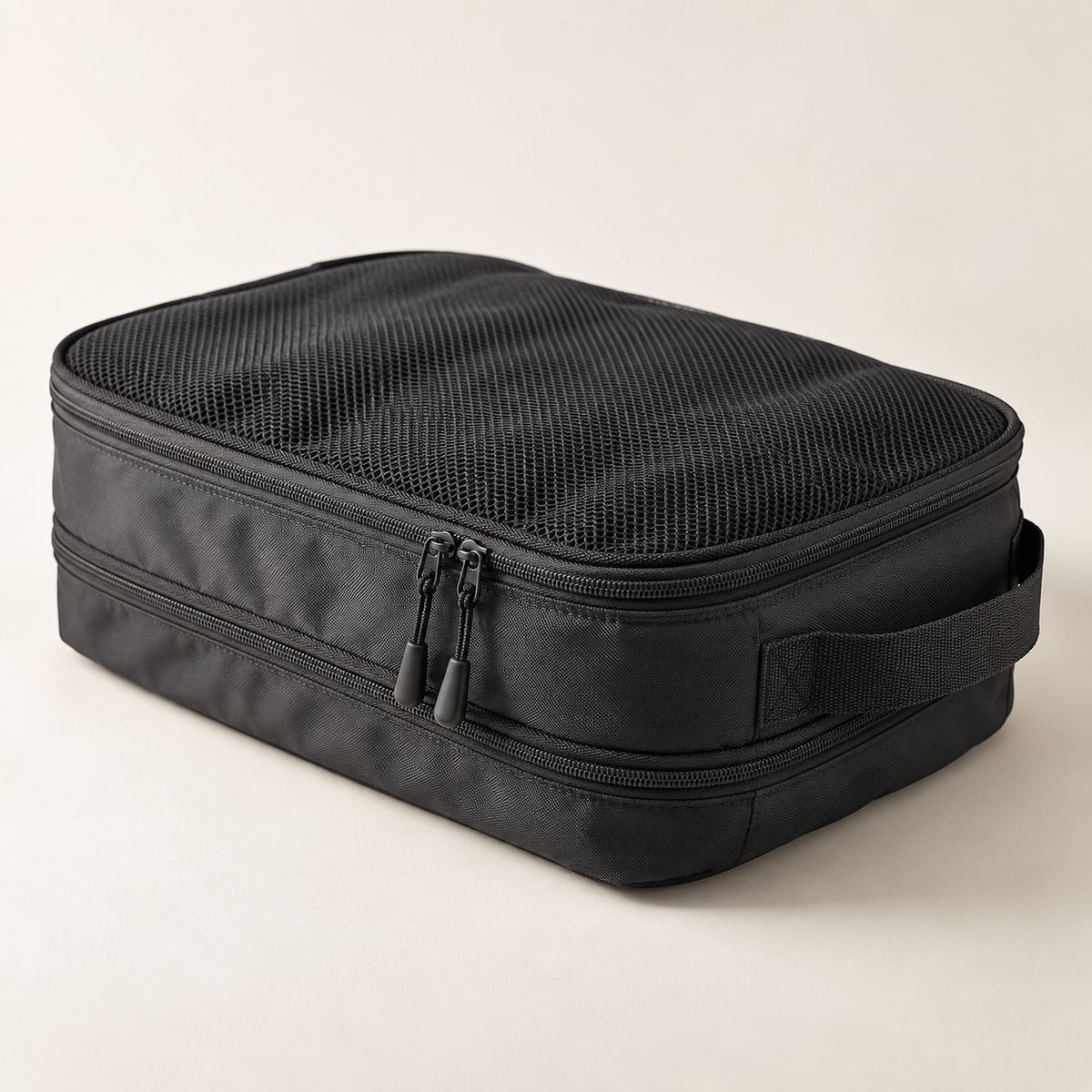 A black rectangular zippered travel organizer bag with a mesh top and side handle, photographed on a clean light beige studio background.