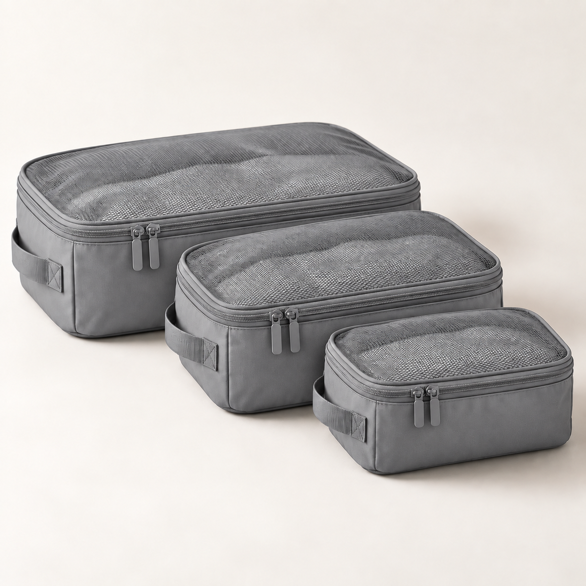 Three gray packing cubes of different sizes arranged diagonally on a light beige background.