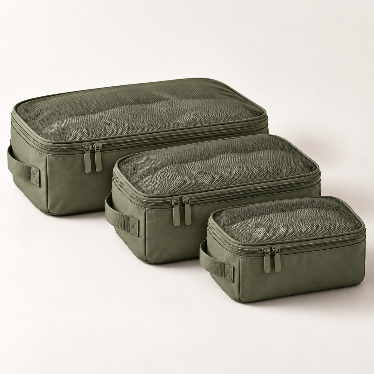Three olive green packing cubes of different sizes arranged diagonally on a light beige studio background.